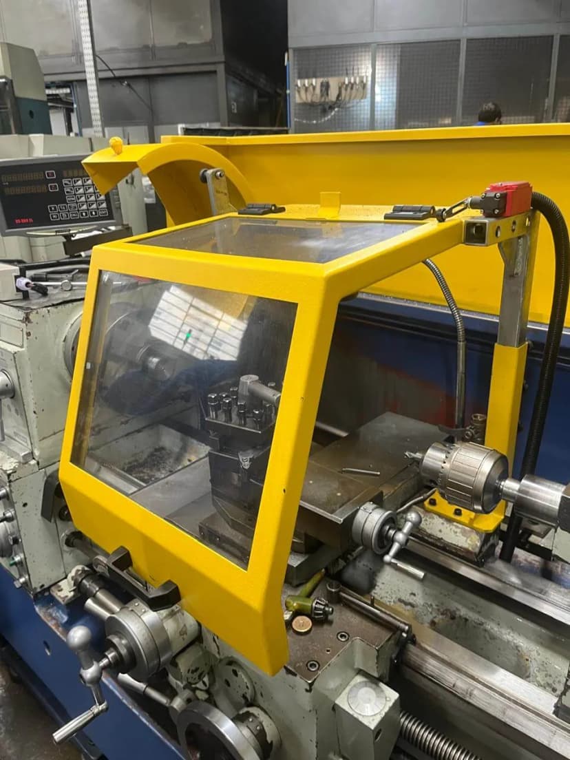 Anteparo móvel transparente com moldura amarela sobre o carro de um torno, monitorado por chave de segurança